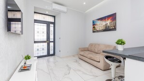 Un soggiorno moderno con un divano, un tavolo da pranzo, una TV a parete e una porta che dà su un'altra stanza.