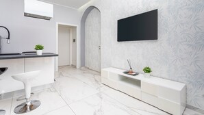Una cucina moderna con un piano di lavoro bianco, uno sgabello da bar, un armadietto bianco e una TV fissata al muro.