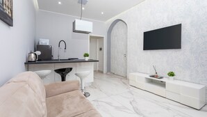 Un soggiorno moderno con divano, TV a parete, angolo cottura con lavello e macchina del caffè, e carta da parati decorata.