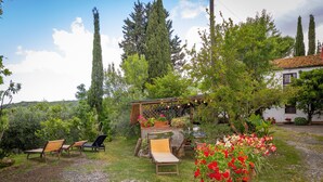 A garden with outdoor seating, a pergola with string lights, and a white building with a tiled roof.