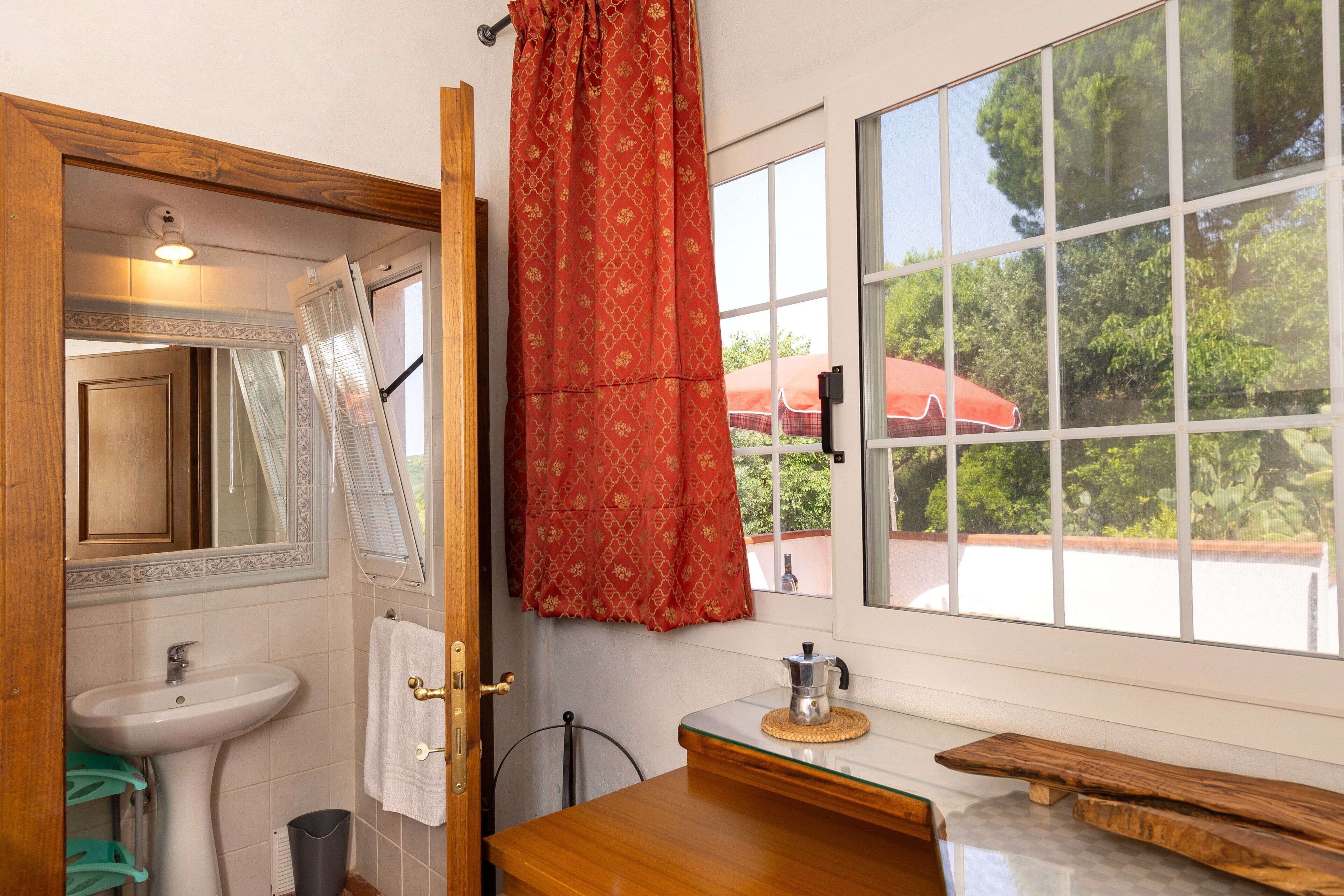 Un baño con lavamanos, espejo y ventana con vistas a la vegetación.