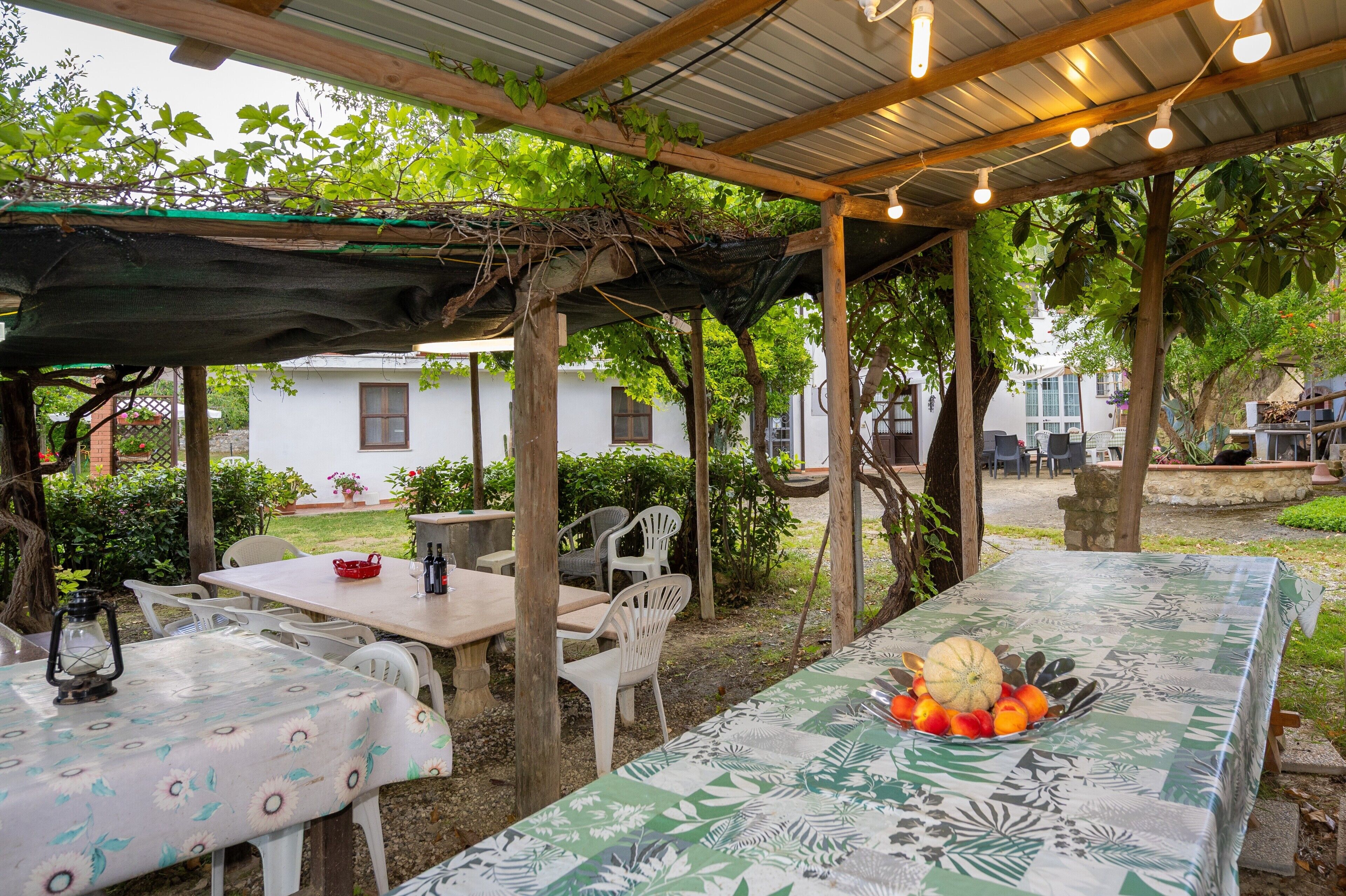 Un patio al aire libre con mesas y sillas, cubierto por una pérgola con luces colgantes.