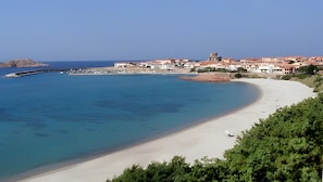 A coastal town with a sandy beach, a rocky outcrop, and a historic tower.