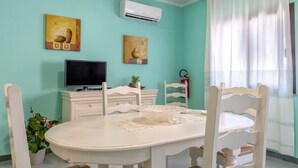 Un comedor con una mesa blanca, sillas, un televisor y obras de arte en las paredes.