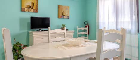 A dining area with a white table, chairs, a television, and artwork on the walls.