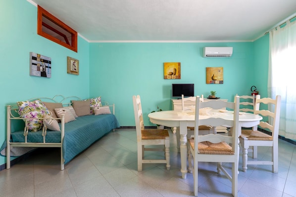 A room with a bed, a dining table with chairs, a TV, and wall art.