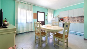 Un comedor con mesa y sillas, una cocina con armarios, un refrigerador y un televisor sobre un mueble.