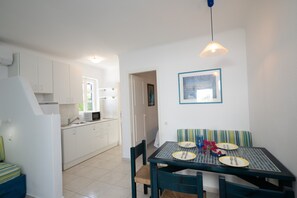 A compact kitchen with white cabinets, a dining table with chairs, and a hanging light fixture.