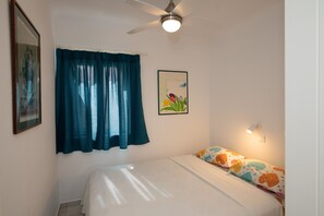 A bedroom with a bed, a ceiling fan, a window with curtains, and a wall-mounted light.