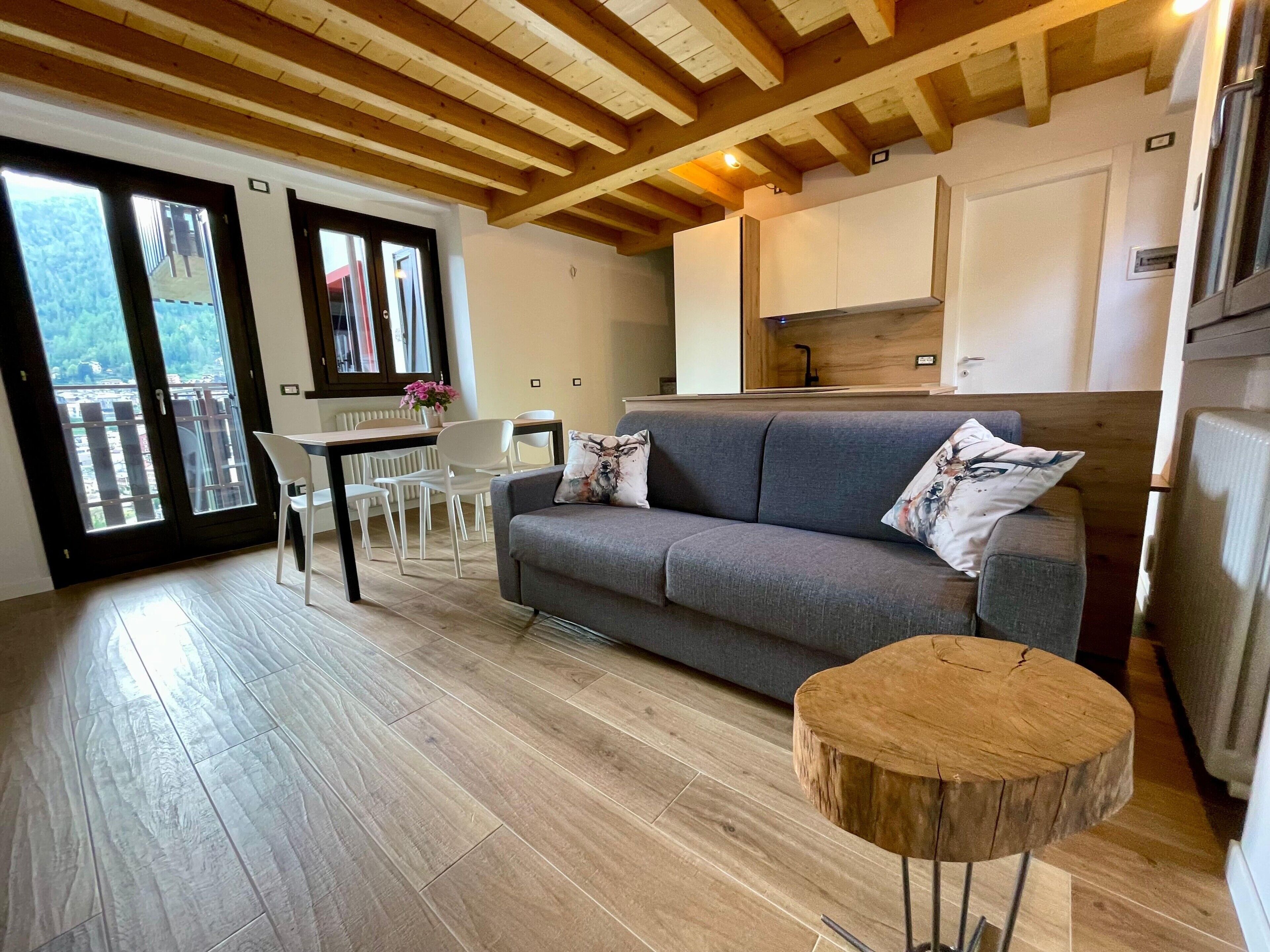 Ein modernes Wohnzimmer mit einem grauen Sofa, einem runden Couchtisch und einem Essbereich mit weißen Stühlen.