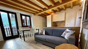 A modern living room with a grey sofa, a round wooden coffee table, and a dining area with white chairs. - “Alpine Dream” Apartment in Valmalenco with Mountain Views and Private Garage (Caspoggio)