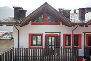 A two-story building with red-framed windows, a balcony with a wooden railing, and a sloped roof. - “Alpine Dream” Apartment in Valmalenco with Mountain Views and Private Garage (Caspoggio)
