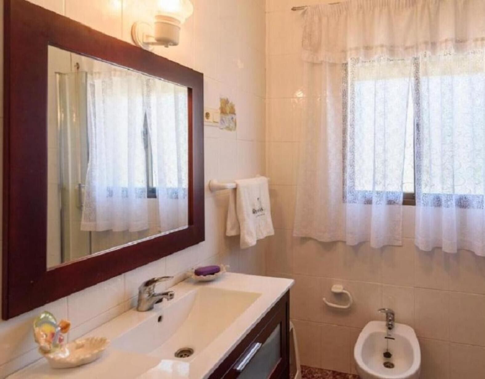 Une salle de bain équipée d’un lavabo, d’un miroir, d’un bidet et d’une fenêtre avec des rideaux.
