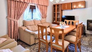 Een gezellige woonkamer met een bank, een eettafel met stoelen, een televisie en een kast.