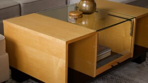 Una sala de estar moderna con una mesa de centro de vidrio, una mesita auxiliar de madera y un sofá.