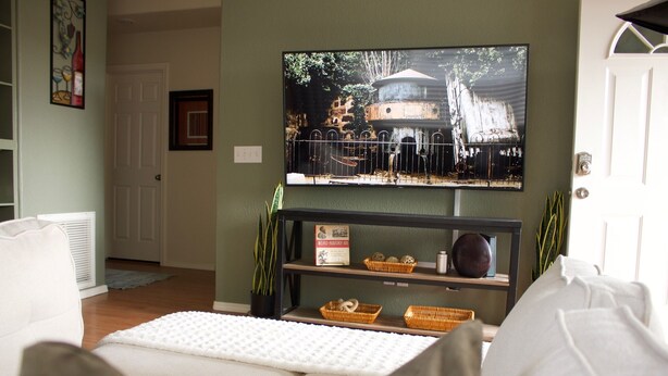 Una sala de estar con una televisión montada en la pared, un sofá, una mesa de centro y una estantería con objetos decorativos.