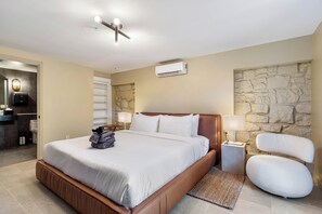 Ett modernt hotellrum med en stor säng, en vägg med dekorativa stenar, en inbyggd luftkonditioneringsanläggning och en sittgrupp med en stol och ett sidobord.