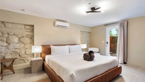 Ein modernes Schlafzimmer mit einer Wand aus Stein, einem großen Bett mit weißen Leinentüchern, zwei Nachttischlampen und einem Deckenventilator.