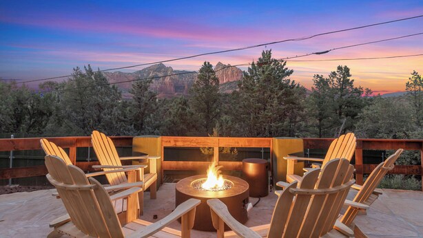 Eine Terrasse mit Holzstühlen und einem zentralen Feuerkorb, mit Blick auf eine gebirgige Landschaft.