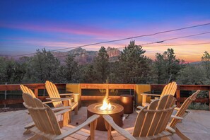 Une terrasse dotée de chaises en bois et d’un foyer central, offrant une vue sur un paysage montagneux.