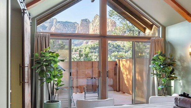 A spacious bedroom with a large bed, a sliding glass door leading to an outdoor patio with a chair and a table, and two potted plants. - Escape to Sedona Demir Suite 205, a cozy 1-bed condo in vibrant Uptown Sedona! (Sedona)