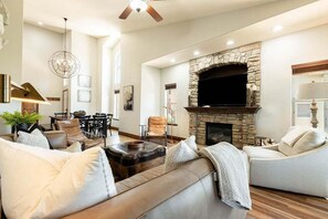 A living room with a stone fireplace, leather sofas, a dining area, and a ceiling fan.