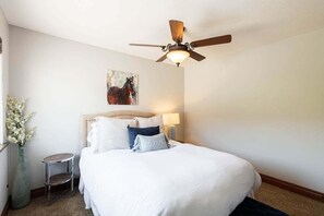 Une chambre à coucher avec un lit, un ventilateur de plafond, une lampe de chevet, une petite table ronde et un vase avec des fleurs.