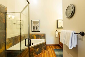 A modern bathroom with a glass-enclosed shower, a bathtub, a framed picture on the wall, a towel rack, and a clock.