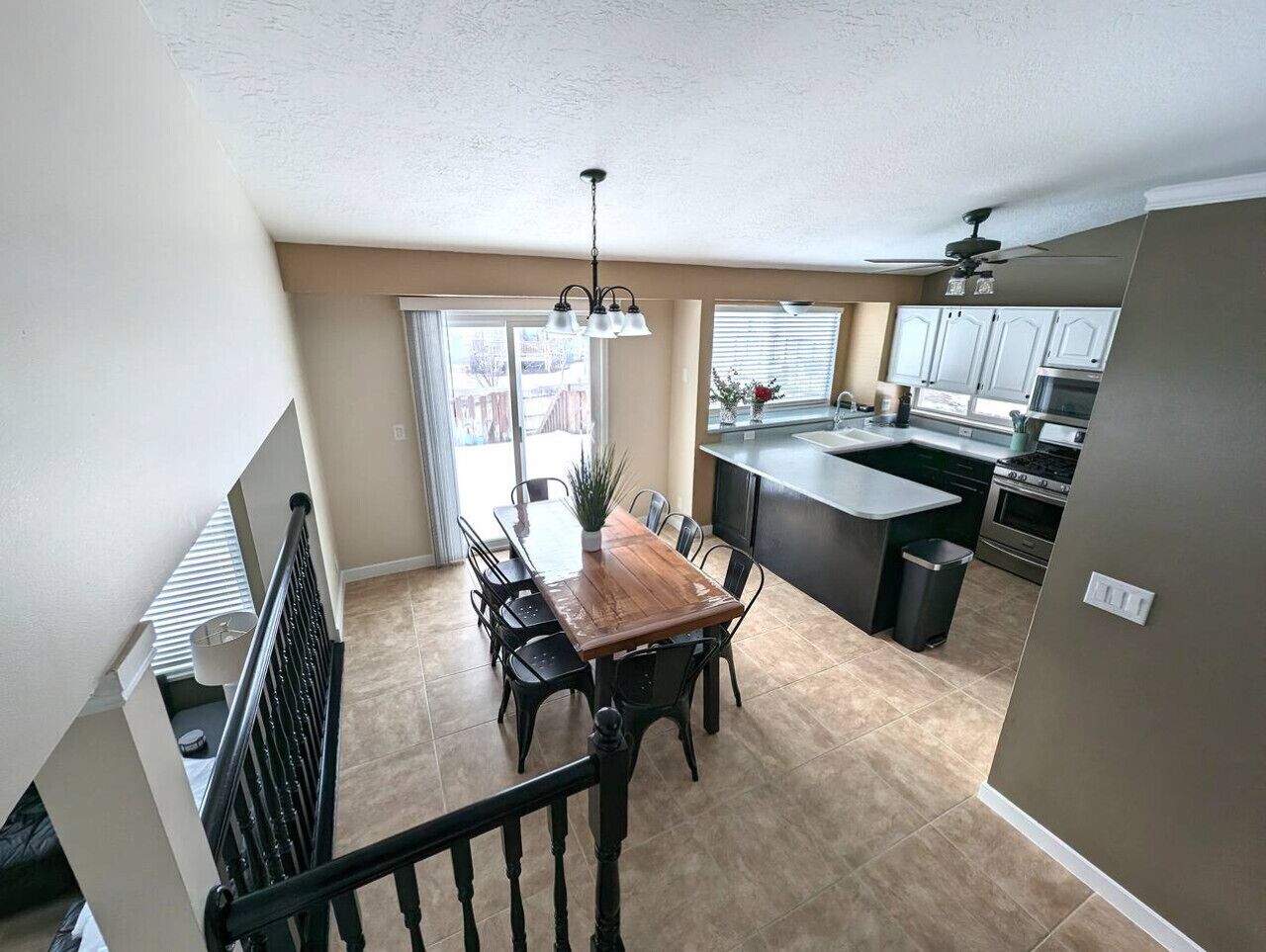 A spacious kitchen with a dining area, large windows, and a ceiling fan.