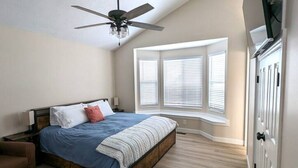 Ein Schlafzimmer mit einem Bett, einem Deckenventilator, einem Fenster mit Jalousien und einem Kleiderschrank.