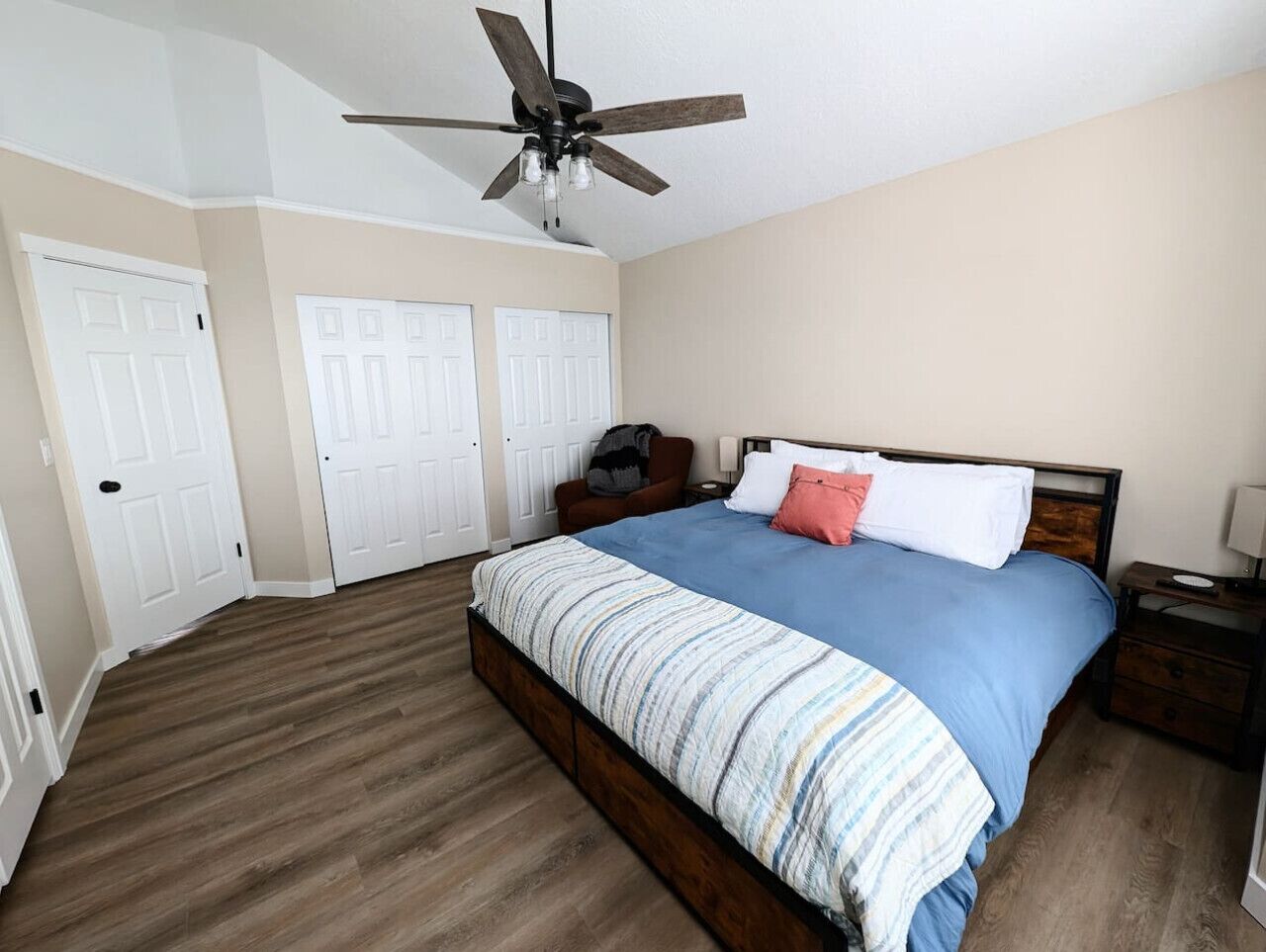 A bedroom with a bed, a ceiling fan, and a wooden floor.