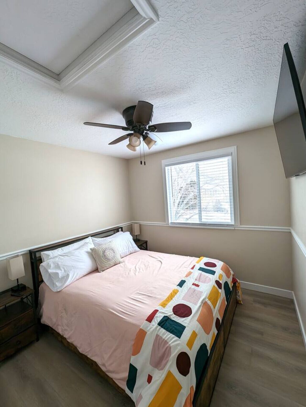 A bedroom with a bed, a ceiling fan, a window, and a nightstand.
