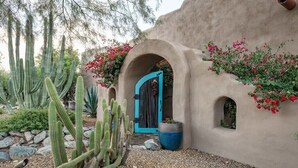 Un bâtiment recouvert d’enduit, avec une porte bleue, des cactus et des plantes en fleurs.