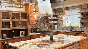 Une cuisine avec des meubles en bois, un îlot en marbre, des luminaires suspendus et un pare-feu.
