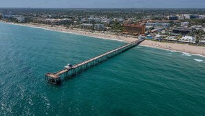 An aerial view of a coastal city with a long pier extending into the ocean, a beach, and various buildings along the shore. - Pet friendly house with a heated pool and hot tub! (Deerfield Beach)