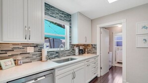 A modern kitchen with white cabinets, a tiled backsplash, and a window overlooking a backyard. - Pet friendly house with a heated pool and hot tub! (Deerfield Beach)
