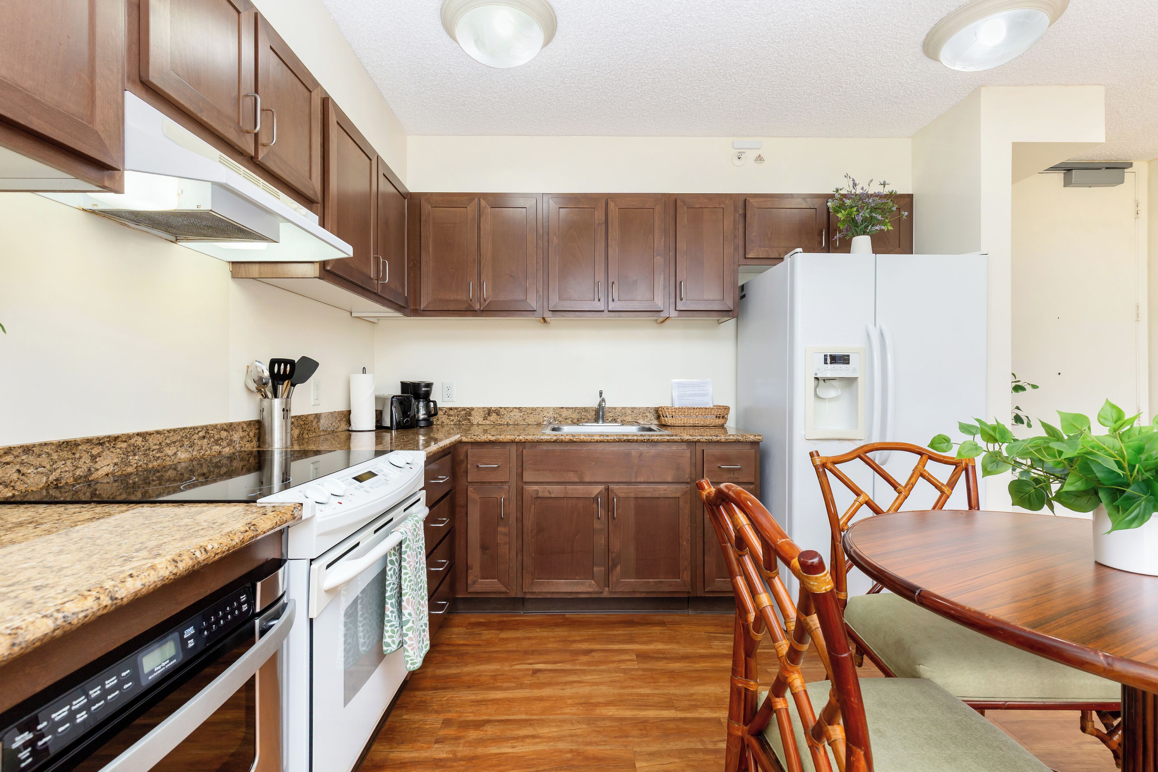 A kitchen with wooden cabinets, a granite countertop, a white refrigerator, and a dining table with chairs.