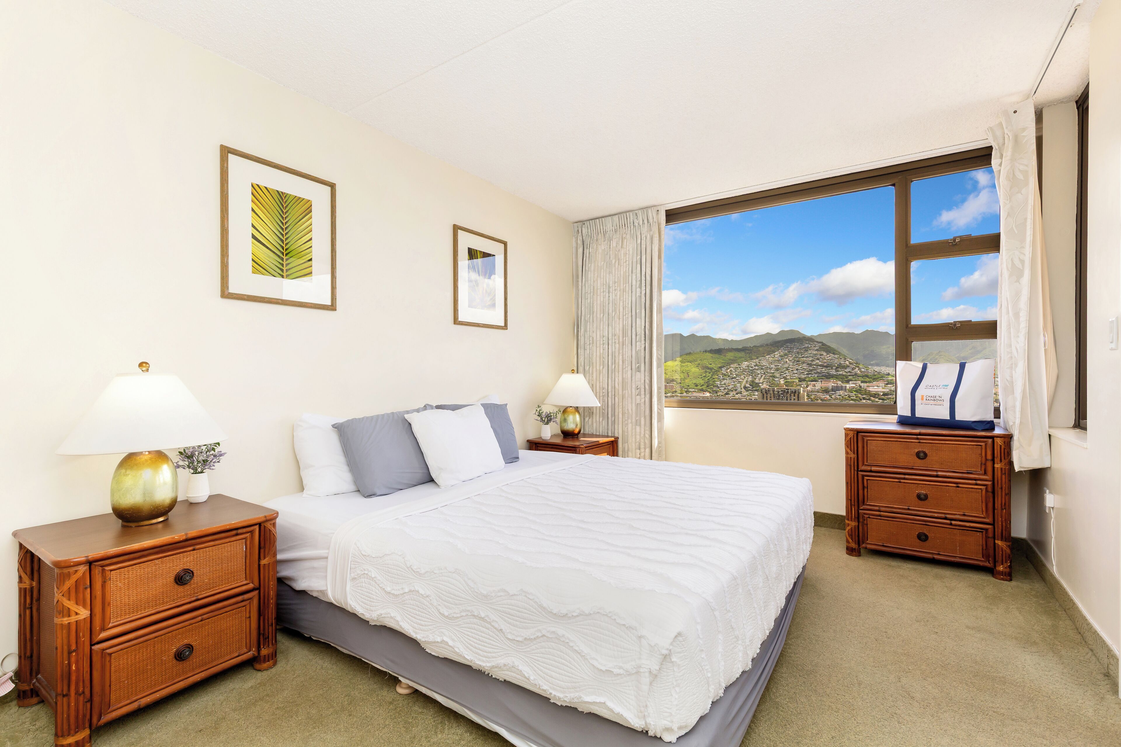 Un dormitorio con una cama grande, dos mesitas de noche, un ventanal con vistas a las montañas y dos cuadros enmarcados en la pared.