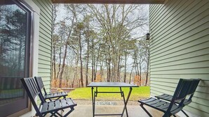 Eine überdachte Terrasse mit zwei Klappstühlen und einem Tisch, mit Blick auf eine Rasenfläche mit Bäumen.