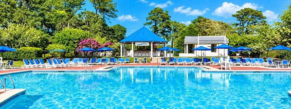 A swimming pool with blue umbrellas and lounge chairs, surrounded by trees and a gazebo.