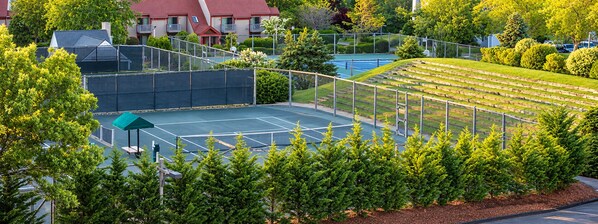 A tennis court surrounded by trees and a residential building.