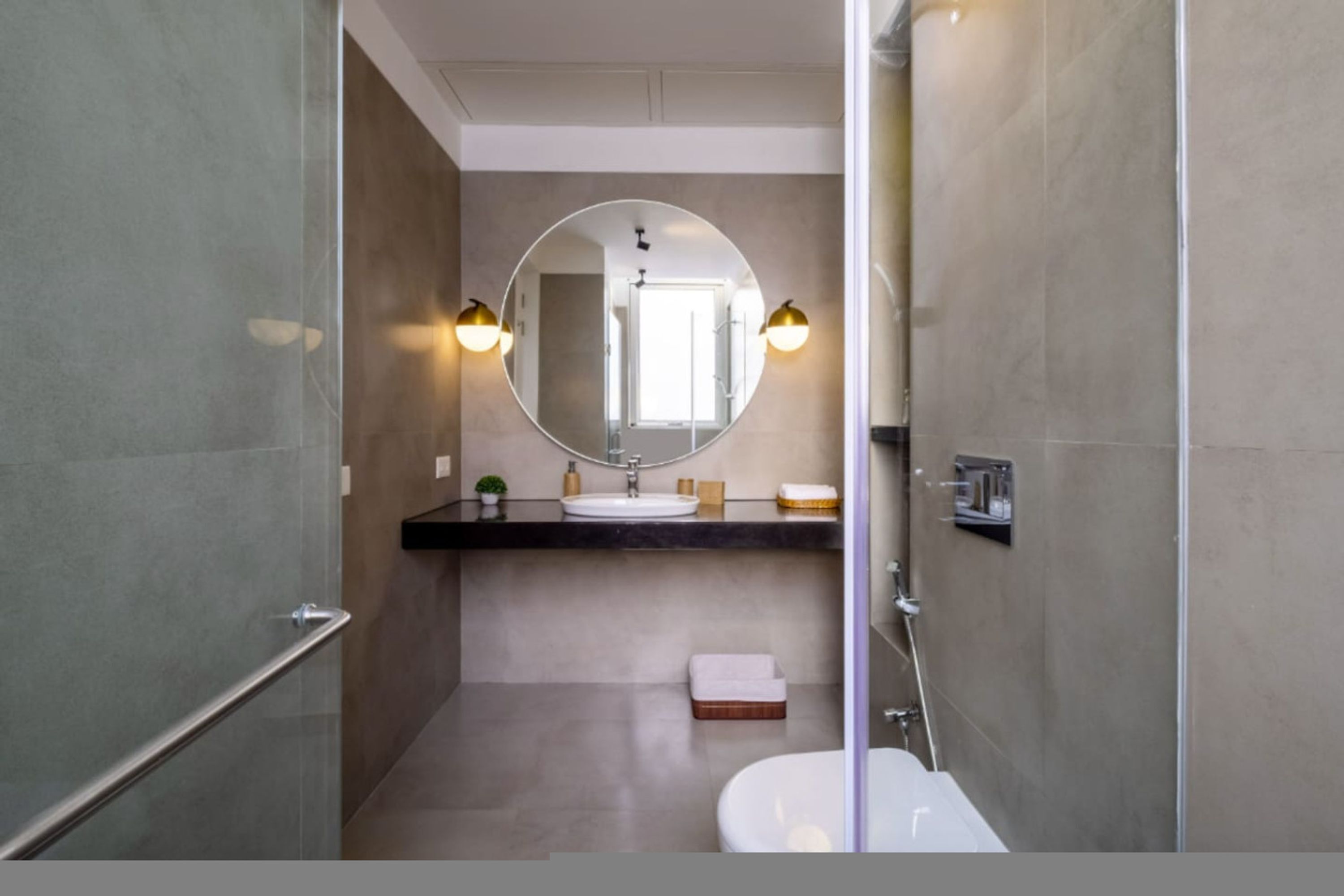 Une salle de bain moderne avec une douche à parois de verre, un miroir rond et un lavabo blanc.