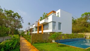 A modern residential building with a swimming pool, surrounded by lush greenery and a wooden fence. - El Rocio - 19 in Assagao (Assagao)