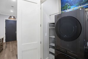 A compact laundry room with a large black washing machine, a dryer, and a shelving unit.