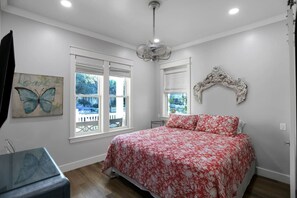 A bedroom with a bed, two windows, a ceiling fan, and a wall-mounted decorative headboard.