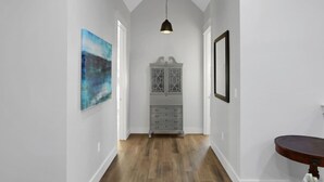 A hallway with a wooden floor, a cabinet with glass doors, and a pendant light. - Large Group Stay | Pool + Walk to Beach (Destin)