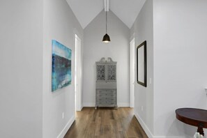 A hallway with a wooden floor, a cabinet with glass doors, and a pendant light. - Large Group Stay | Pool + Walk to Beach (Destin)