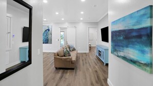 A spacious living room with a beige sofa, a light blue cabinet, and a large abstract painting on the wall. - Large Group Stay | Pool + Walk to Beach (Destin)