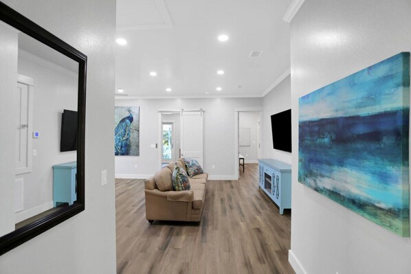 A spacious living room with a beige sofa, a light blue cabinet, and a large abstract painting on the wall.