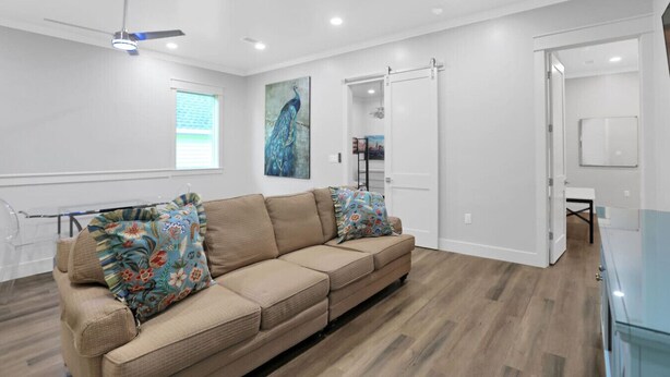 Un salon spacieux avec un canapé d’angle beige, un ventilateur de plafond et une grande fenêtre.